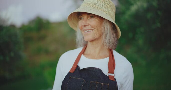 Portrait of happy mature woman in her 60s smiling, tending to her garden in the golden years of retirement