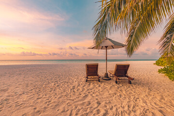 Summer beach landscape. Luxury vacation and holiday concept, summer travel banner. Panoramic landscape of sunset beach, two loungers umbrella, palm leaf, colorful sunset sky for paradise island view