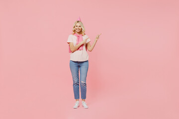 Full body elderly happy woman 50s in t-shirt birthday hat point index finger aside on workspace area mock up isolated on plain pastel pink background studio portrait Celebrating party holiday concept