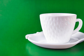 A beautiful white cup (mug) in the shape of a strawberry stands on a saucer on a green background. Space for text. Empty clean dishes.