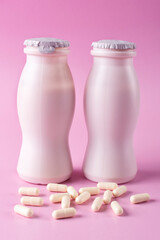 Two bottles of milk yogurt (kefir) and capsules with probiotic on a pink background. The concept of an alternative to pills and a healthy diet. Vertical photo.