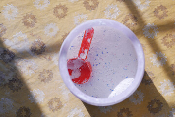 Washing powder in plastic spoon on blue background 