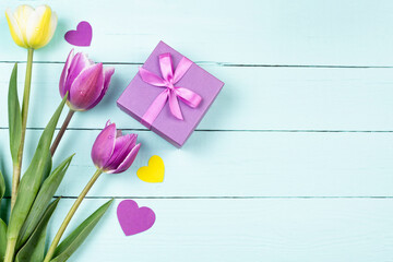 Yellow and lilac flowers tulips, a gift box and hearts on a wooden blue background. Holidays: March 8, Valentine's Day, birthday. Space for text.