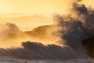 Stock photo of strong waves breaking against rocks on a beach in Iceland at sunset. 