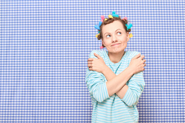 Portrait of happy dreamy young woman with bright hair curlers on head