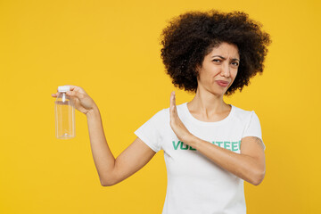 Young sad woman of African American ethnicity wears white volunteer t-shirt refuse plastic pet bottles say no isolated on plain yellow background. Voluntary free work assistance help charity concept.