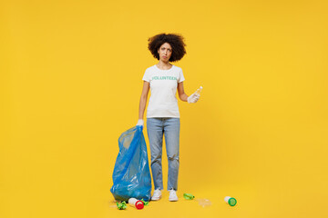 Full body young woman of African American ethnicity wears white volunteer t-shirt hold trash bag...