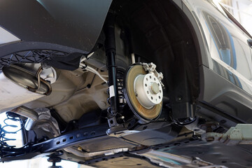 Car in a car service on a lift. The rear wheel has been removed from the car. Brake disc, suspension elements. Selected focus. 