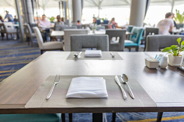 Restaurant table setting. Empty white plate, white napkin, knife and cutlery on the table. Table top counter Bar restaurant background with people