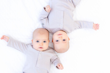 two newborns a twin baby a girl in a cotton suit on a white bed at home are lying and smiling