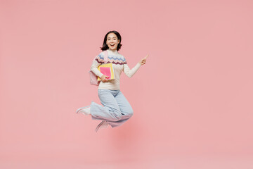 Full body fun teen student girl of Asian ethnicity wear sweater hold backpack jump high point index finger aside isolated on pastel plain light pink background Education in university college concept.