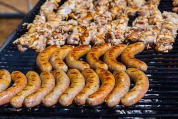 Sausages and meat on a wooden skewers on the grill, close-up.