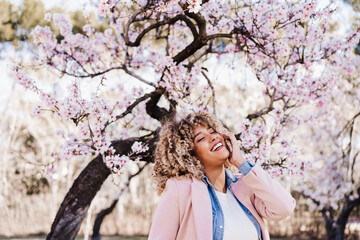 portrait of beautiful hispanic woman with afro hair in spring among pink blossom flowers. nature - 489560149