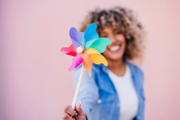beautiful happy hispanic woman with afro hair holding colorful pinwheel. pink background,wind energy