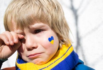 face of a frightened boy, a painted heart on the cheek in yellow-blue colors of the Ukrainian flag....