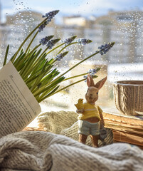 Moscow, Russia, February 2022, Easter card, figurine of a rabbit in a yellow T-shirt, with a blue Easter egg on the background of a book and a window