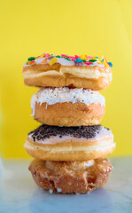 Four color donuts stacked in front of a bright yellow background