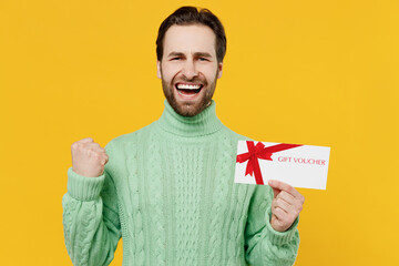 Young happy cool man 20s in mint knitted sweater hold gift certificate coupon voucher card for...