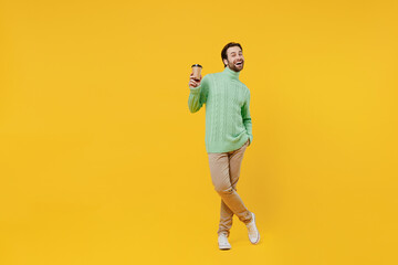 Fototapeta na wymiar Full body smiling happy young man 20s wear mint knitted sweater hold takeaway delivery craft paper brown cup coffee to go isolated on plain yellow background studio People lifestyle fashion concept