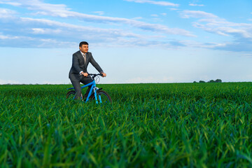 business concept - A businessman rides a bicycle on a green grass field, dressed in a business suit, he has a briefcase and documents