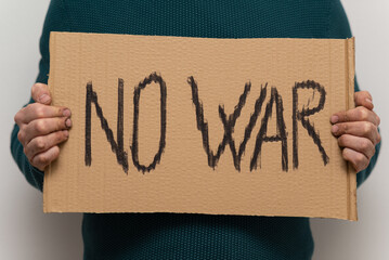 Male dirty hands holding a cardboard with "NO WAR" text written.
