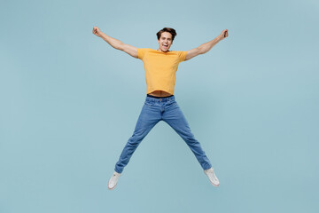 Fototapeta na wymiar Full body overjoyed fun joyful cool young man 20s wear yellow t-shirt jump high with outstretched hands legs isolated on plain pastel light blue background studio portrait. People lifestyle concept.