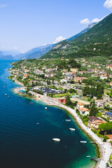 Small mediterranean town Malcesine and lake Garda, Italy, with boats, beach and mountains in the horizon during summer time