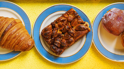 Croissant and puff pastry. Sweet buns on blue plate, yellow background