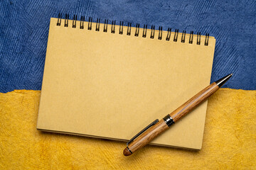 blank notebook with a pen against paper abstract in colors of Ukrainian national flag - blue and yellow