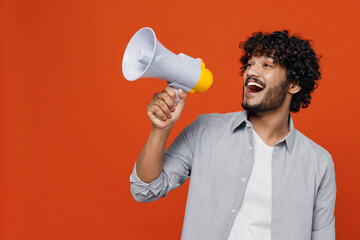 Jubilant overjoyed excited vivid young bearded Indian man 20s years old wears blue shirt hold scream in megaphone announces discounts sale Hurry up isolated on plain orange background studio portrait. - obrazy, fototapety, plakaty