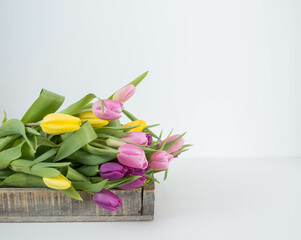 pink, yellow and purple tulips in a wooden tray with space for text
