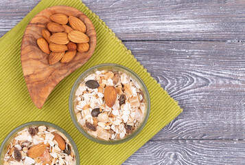 Top view of granola with nuts and dry fruits and almonds in an olive bowl on a green napkin on a gray whitewashed rustic table, copy space. Healthy breakfast
