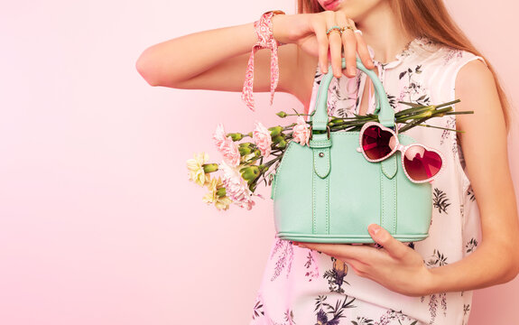 Fashion spring accessories - girl holding mint handbag (purse) and sunglasses on pastel pink.