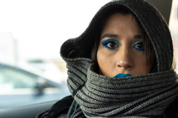 Woman covered in scarf and with blue eyeshadow and lipstick in a car