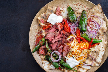 Traditional Greek beef gyros with cabbage carrot salad, yogurt and flat bread served as top view on a rustic wooden board with copy space left