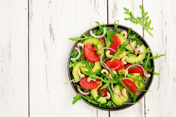 Healthy vegan vegetarian lunch salad with arugula, avocado, grapefruit and cashews and dressing of olive oil, honey and wine vinegar. White rustic kitchen table, top view