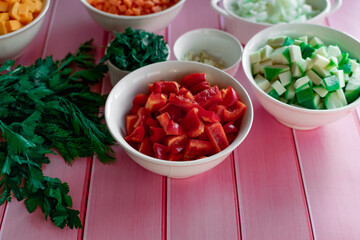Fresh Bulgarian sweet red pepper diced in a bowl, on a pink wooden background, fresh vegetables for cooking in the kitchen, prepared ingredients