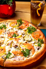 italian pizza with tomatoes, cucumber, chicken and peppers on a table with a cocktail at sunset