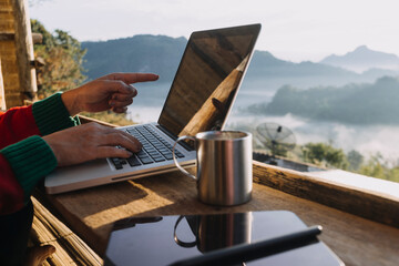 Young business woman working at the computer in cafe on the rock. Young girl downshifter working at a laptop at sunset or sunrise on the top of the mountain to the sea, working day..
