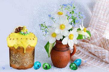 Easter cake decorated with sugar chicken and quail eggs, a bouquet of anemones and forget-me-nots in a clay vase on a light background