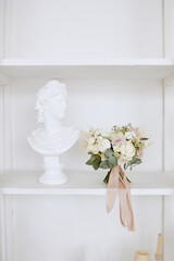 The wedding bouquet is on a white shelf next to a plaster sculpture
