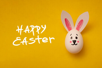Food photo for Easter. Chicken egg with a cute rabbit face and rabbit ears on a yellow background. Greeting card for Easter holiday. Happy Easter text. Preparation for the celebration. Family holiday