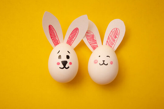 Photo of food for Happy Easter. Chicken eggs with cute bunny faces and rabbit ears on a yellow background. Preparation for the holiday. Greeting card for Easter holiday.