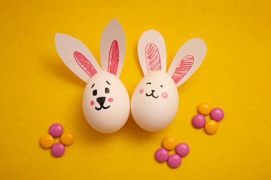 Food photo for Happy Easter. Chicken eggs with cute bunny faces and bunny ears and yellow and pink candies on a yellow background. Preparation for the holiday. Greeting card for Easter holiday.