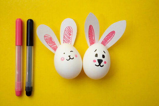 Photo of food for Happy Easter. Chicken eggs with cute bunny faces and rabbit ears and felt-tip pens on a yellow background. Preparation for the holiday. Greeting card for Easter holiday.