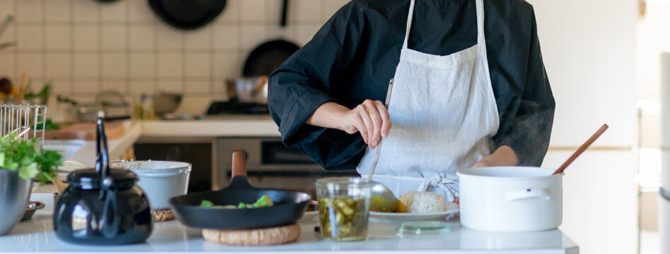 キッチンで料理をするエプロン姿の女性　皿に料理を盛り付ける