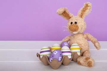 Easter composition - a rabbit and colorful eggs on a lilac background.