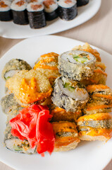 Fried rolls of different types lie on a plate with red ginger leaves. Close-up, selective focus. Vertical photo.