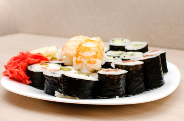 Sushi with tiger shrimp, rolls with salmon and cucumber and ginger lie on a plate. Close-up, selective focus.