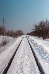 Fototapeta na wymiar Railway going to the perspective. Powerlines and trees nearby. Snowy winter landscape